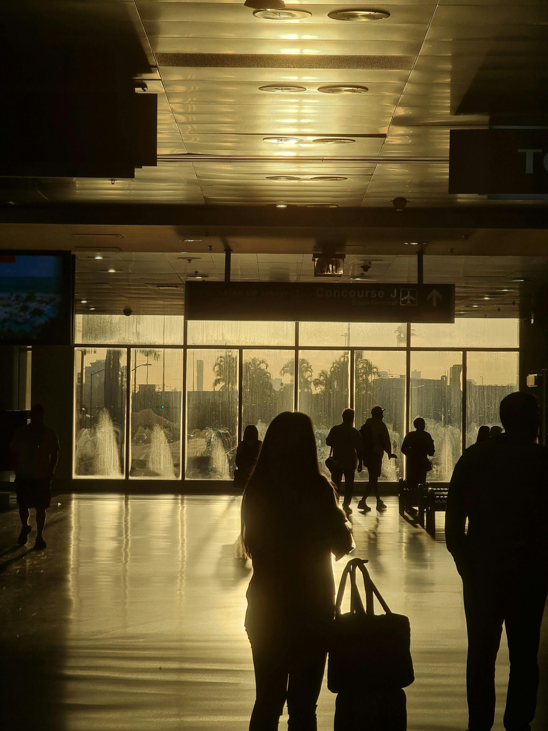 Silhouetted travelers walk through a sunlit Miami airport terminal, creating a vibrant play of light and shadow.